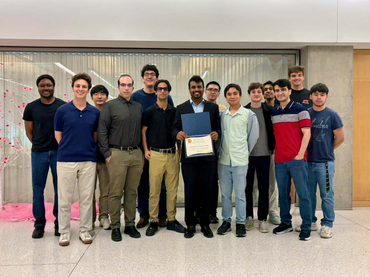 Maneesh holds his Outstanding Graduate Teaching Assistant Award certificate, surrounded by students and lab members.