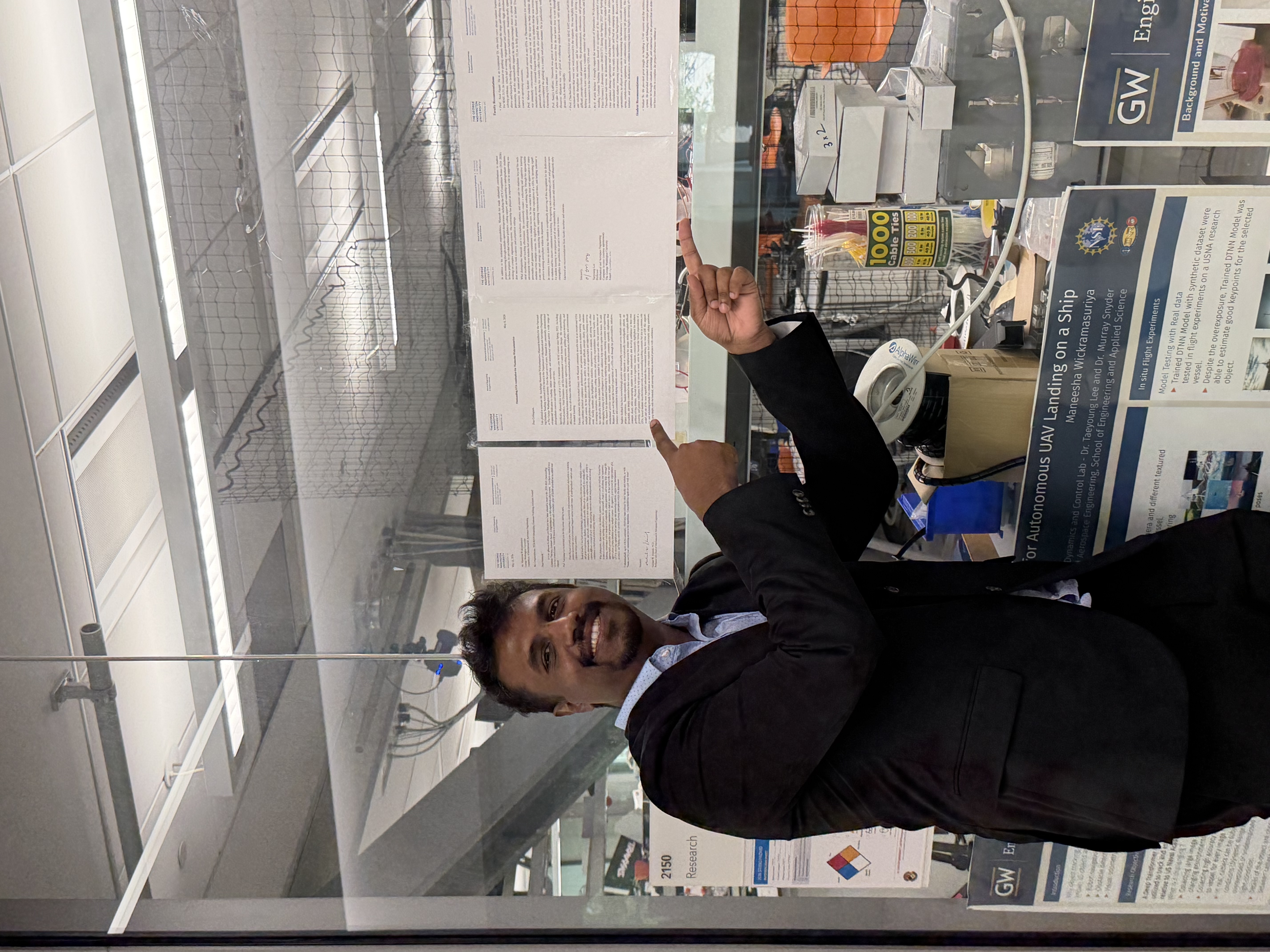 Maneesh points to nomination letters and messages of appreciation displayed on the lab windows.